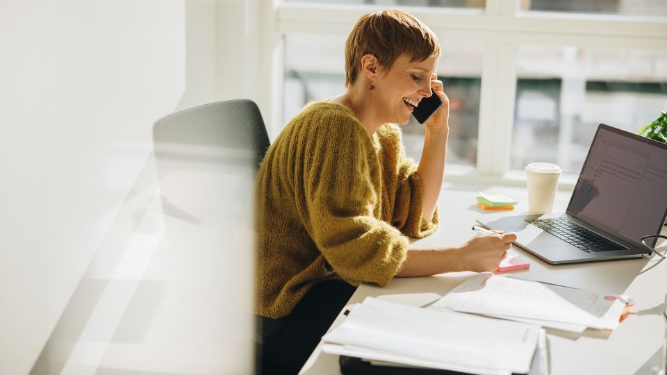 Eine Frau sitzt in einem hellen Büro an einem Computer und telefoniert.